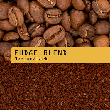 Coffee photograph showing whole roasted coffee beans at the top, roasted coffee grounds at the bottom, and a black label across the center reading “FUDGE BLEND” and “Medium/Dark”.