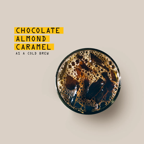one glass of cold coffee brew on a beige background, with text reading: Chocolate, Almond, Caramel tasting notes 