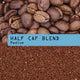 Coffee photograph showing whole roasted coffee beans at the top, roasted coffee grounds at the bottom, and a pastel blue label across the center reading “Half caf blend” and “Medium”.