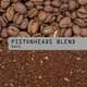 Coffee beans on top and brewed coffee granules below, with a gray label across the center reading 'PISTONHEADS BLEND Dark'.