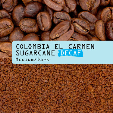 A close-up product Photo of decaf coffee showing whole roasted coffee beans at the top, a light blue label across the center reading 'COLOMBIA EL CARMEN SUGARCANE DECAF Medium/Dark', and ground coffee below.