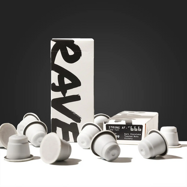A white box labeled RAVE, featuring Strong AF Blend Coffee Pods, sits against a dark gray background with several gray and white Nespresso compatible pods scattered in front. The box’s side reads STRONG AF - 666 along with flavor notes below.